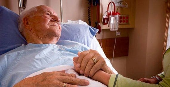 Old man lying in hospital bed holding daugher Similarities between COVID-19 deaths, severe rheumatic illnesses