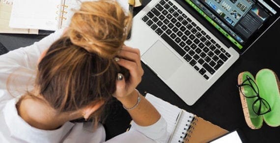 Stressed woman holding her head, staring down at her desk Success strategies for working through chronic stress
